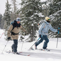 Två turåkare går med skidor genom snöig skog