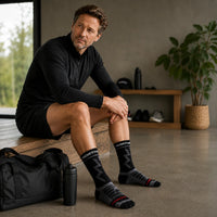 Man wearing black compression sports socks while sitting after a workout in a gym.